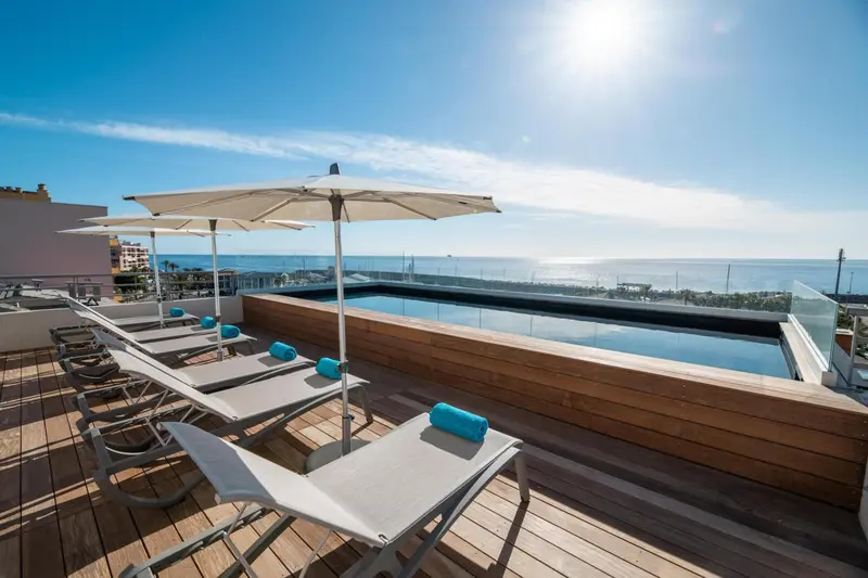 Terrasse avec transats et piscine au bord d'une mer bleue.