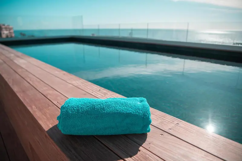 Une serviette turquoise est posée sur le bord d'une piscine à débordement avec vue sur la mer.