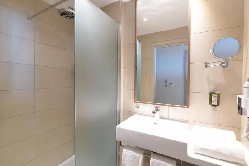 Une salle de bain claire avec douche à l'italienne et grand miroir.