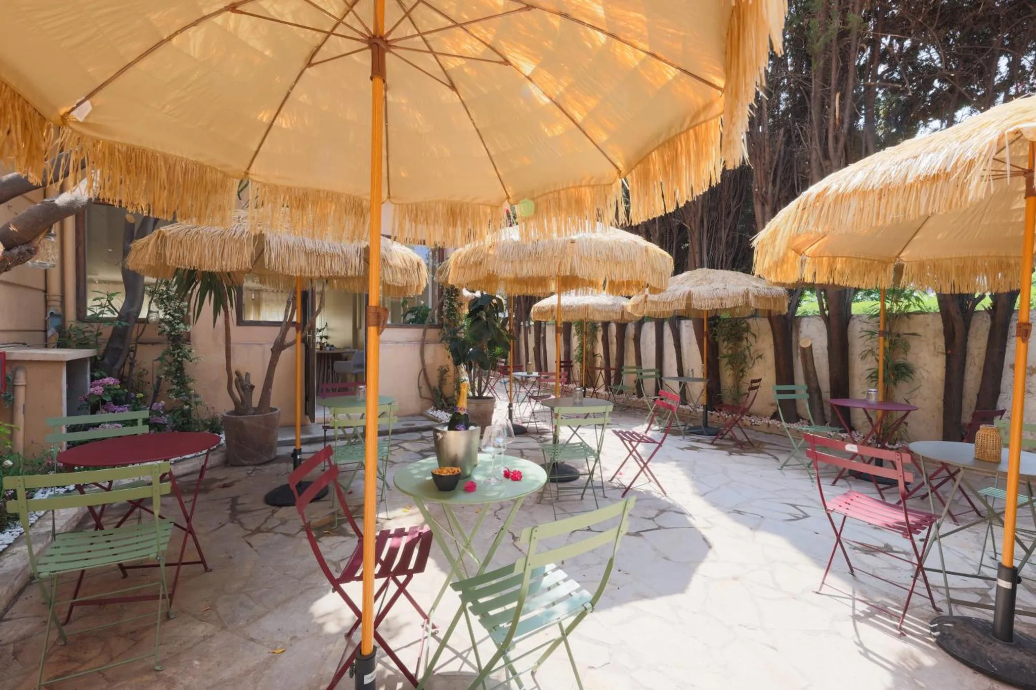 Terrasse ombragée avec tables et chaises colorées.
