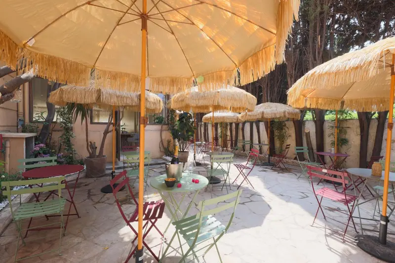 Terrasse ombragée avec tables et chaises colorées.