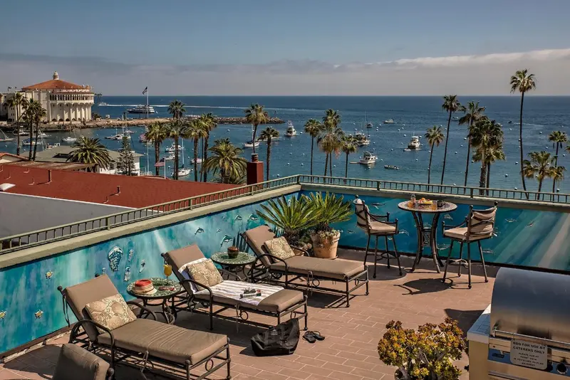 Terrasse aménagée avec chaises longues et tables, vue sur la mer et le port.