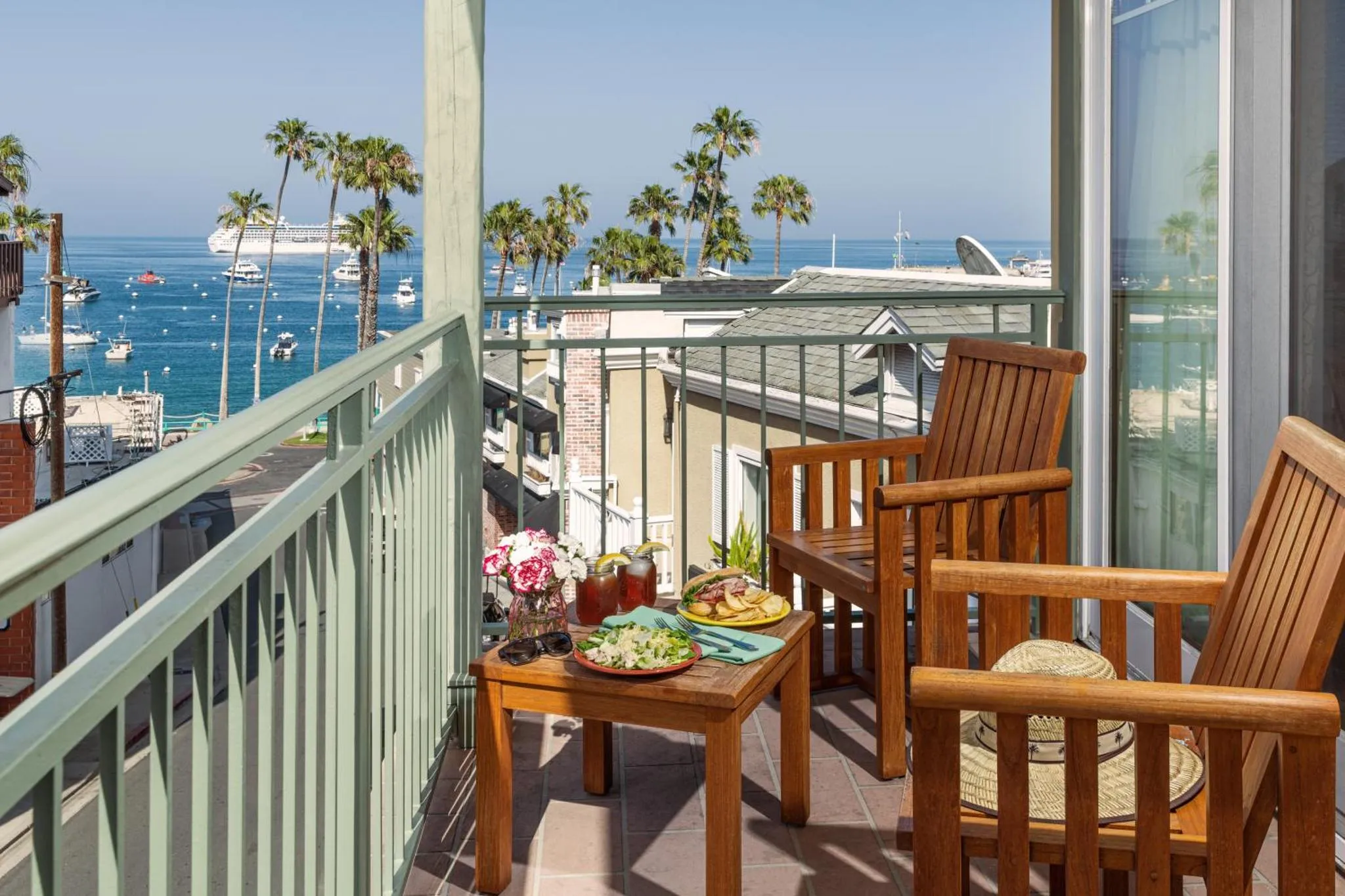 Une table basse avec des plats et des boissons sur un balcon avec vue sur la mer et des bateaux.