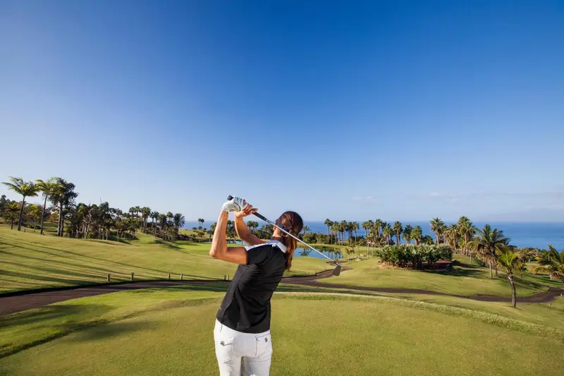 Une personne frappe une balle de golf sur un terrain verdoyant face à la mer.