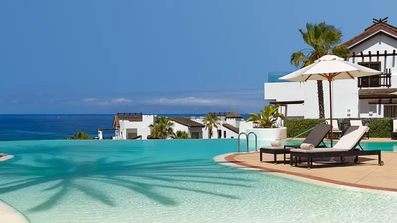 Transats et parasols bordent une piscine à débordement avec vue sur la mer.