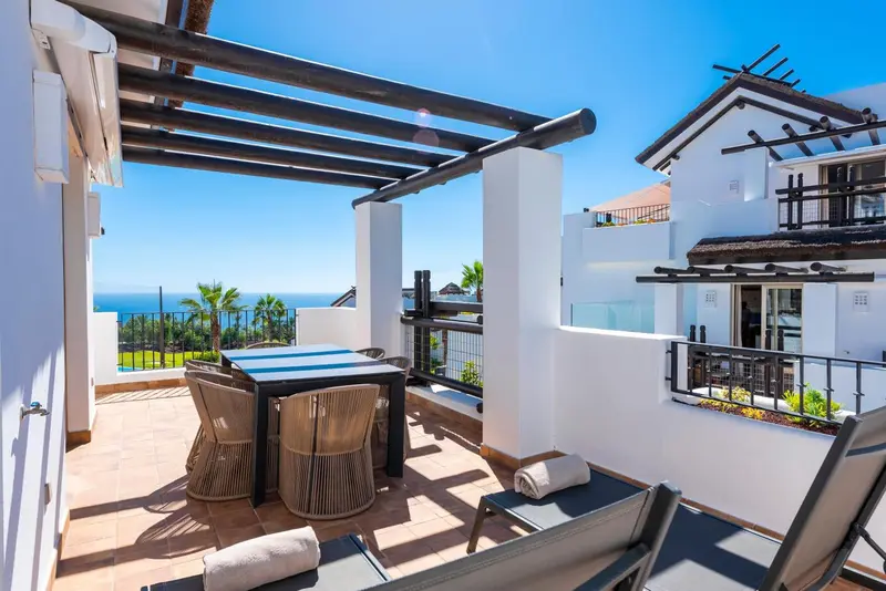 Terrasse carrelée avec mobilier de jardin et vue sur la mer.