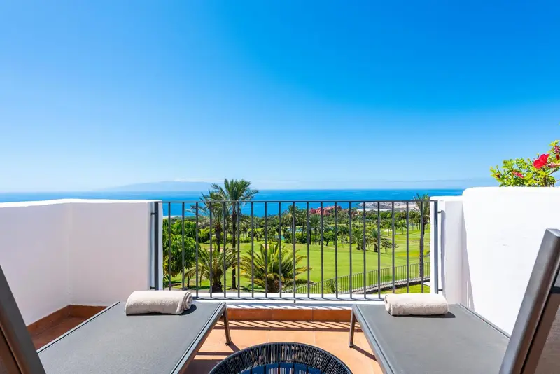 Deux transats sur une terrasse avec vue sur un paysage verdoyant et la mer.