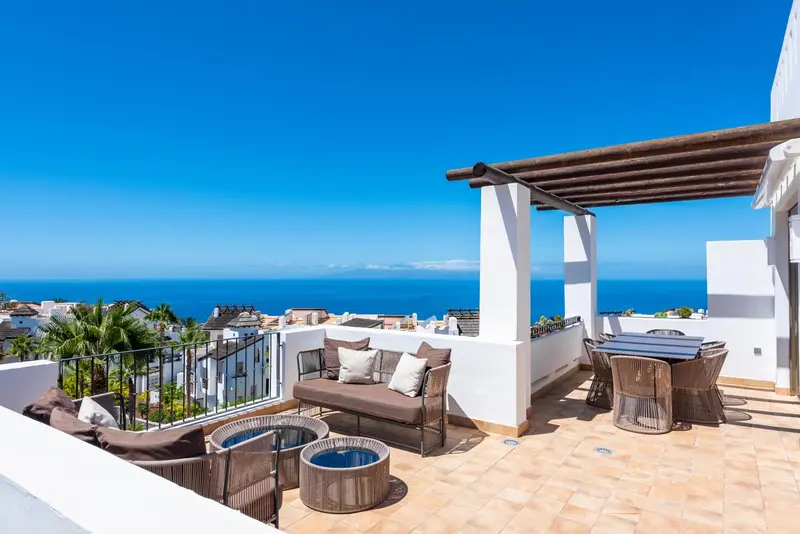 Terrasse aménagée avec salon et table, vue sur la mer et le littoral.