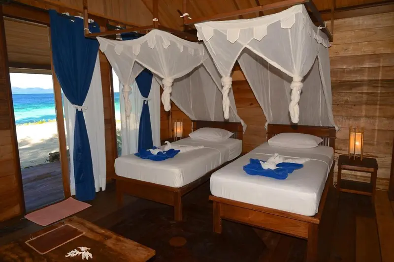 Deux lits simples dans une chambre en bois avec moustiquaires et vue sur la mer.