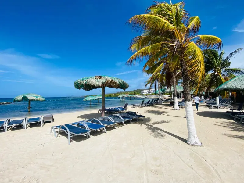 Plage de sable blanc avec transats et parasols sous un ciel bleu.