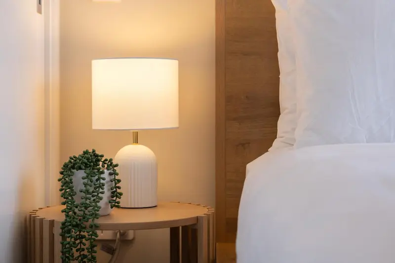 Une lampe de chevet illumine un lit blanc.
