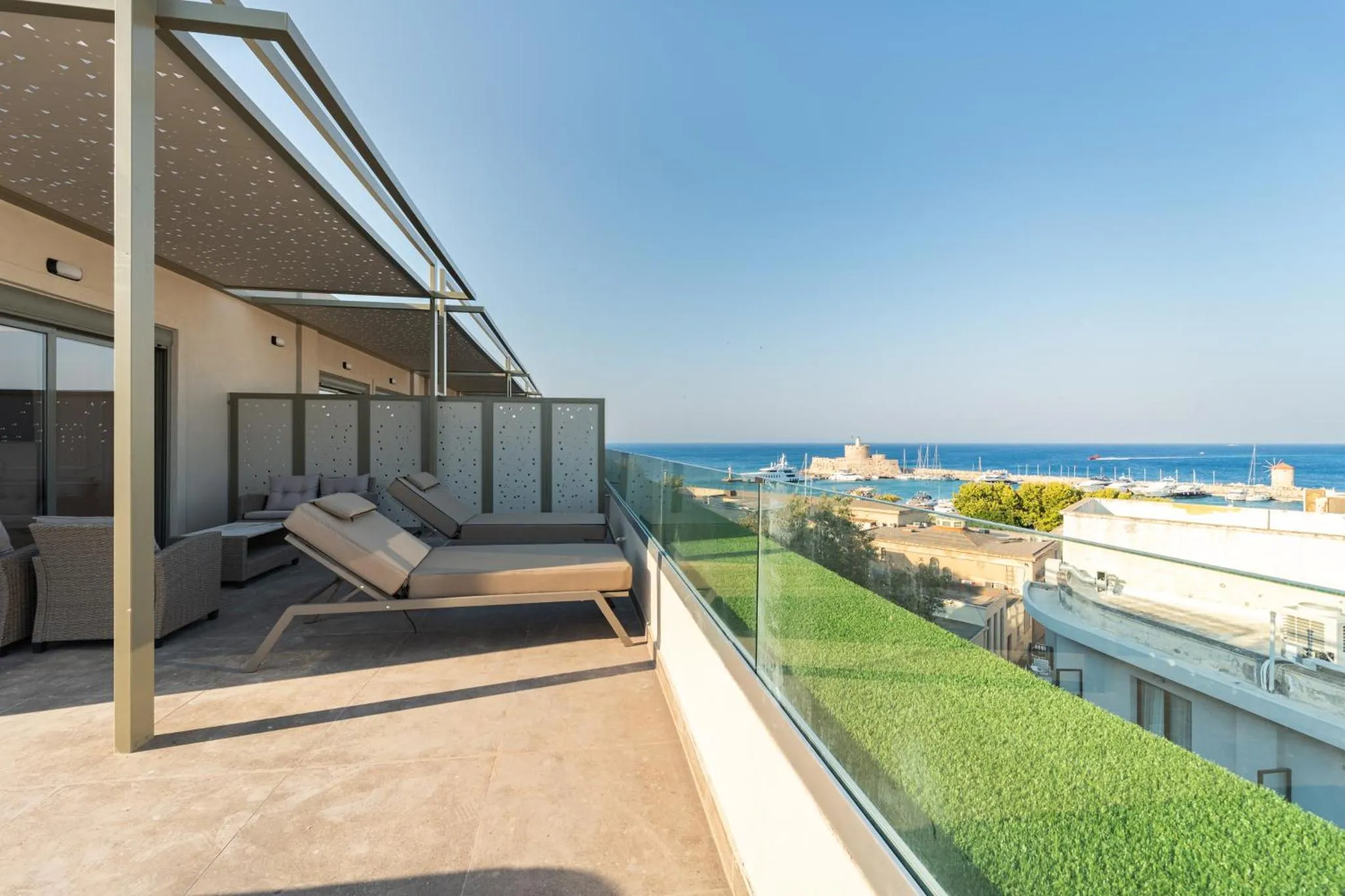 Terrasse avec transats et vue sur la mer et un port.