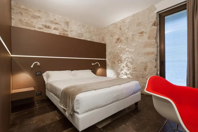 Une chambre moderne avec un lit blanc et un mur en pierre.