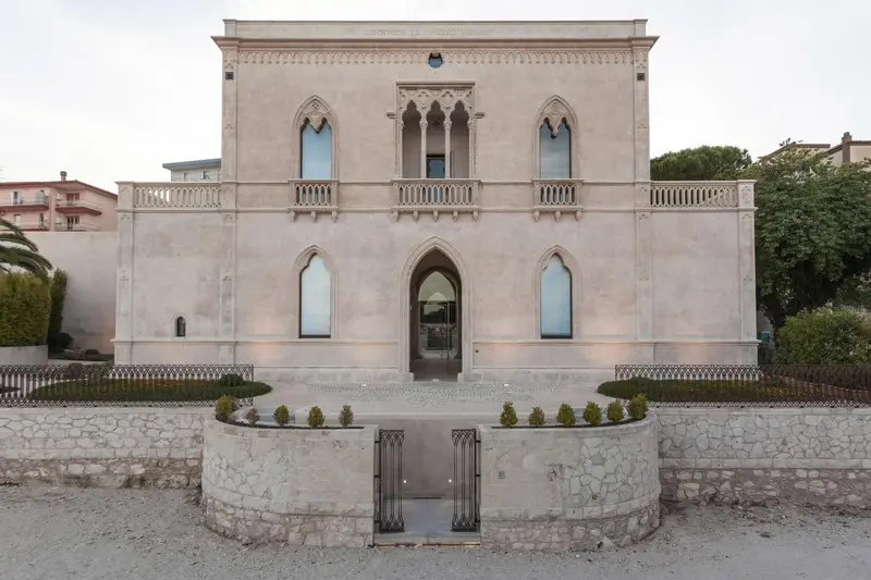 Facade d'un bâtiment à l'architecture néo-gothique avec un jardin soigné.