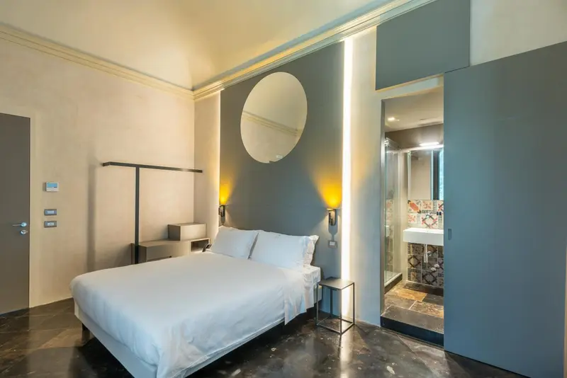 Une chambre moderne avec un lit blanc et un grand miroir rond au mur.