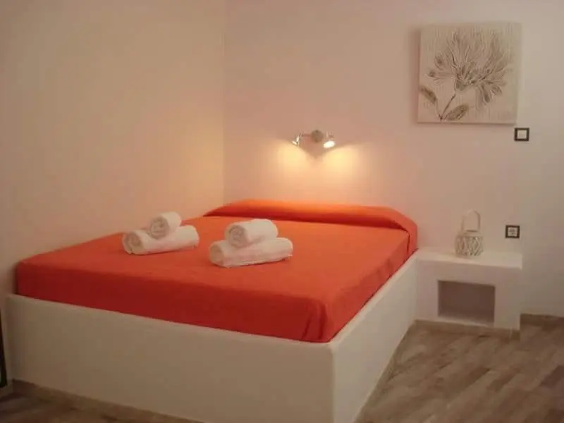 Une chambre lumineuse avec un grand lit recouvert d'une couverture orange et des serviettes roulées.