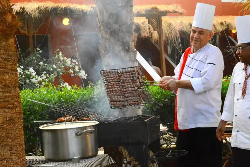Un chef prépare de la viande grillée devant un buffet extérieur.