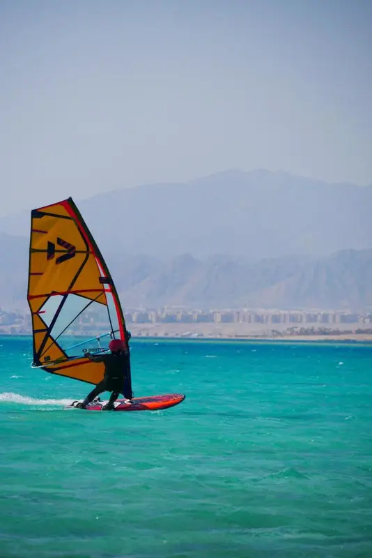 Un pratiquant de planche à voile glisse sur une mer turquoise sous un ciel bleu.