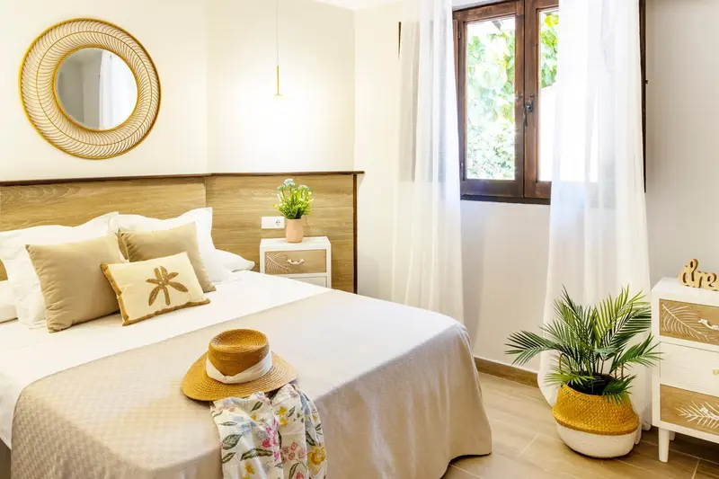 Une chambre lumineuse avec un grand lit recouvert de coussins et d'un chapeau de paille.