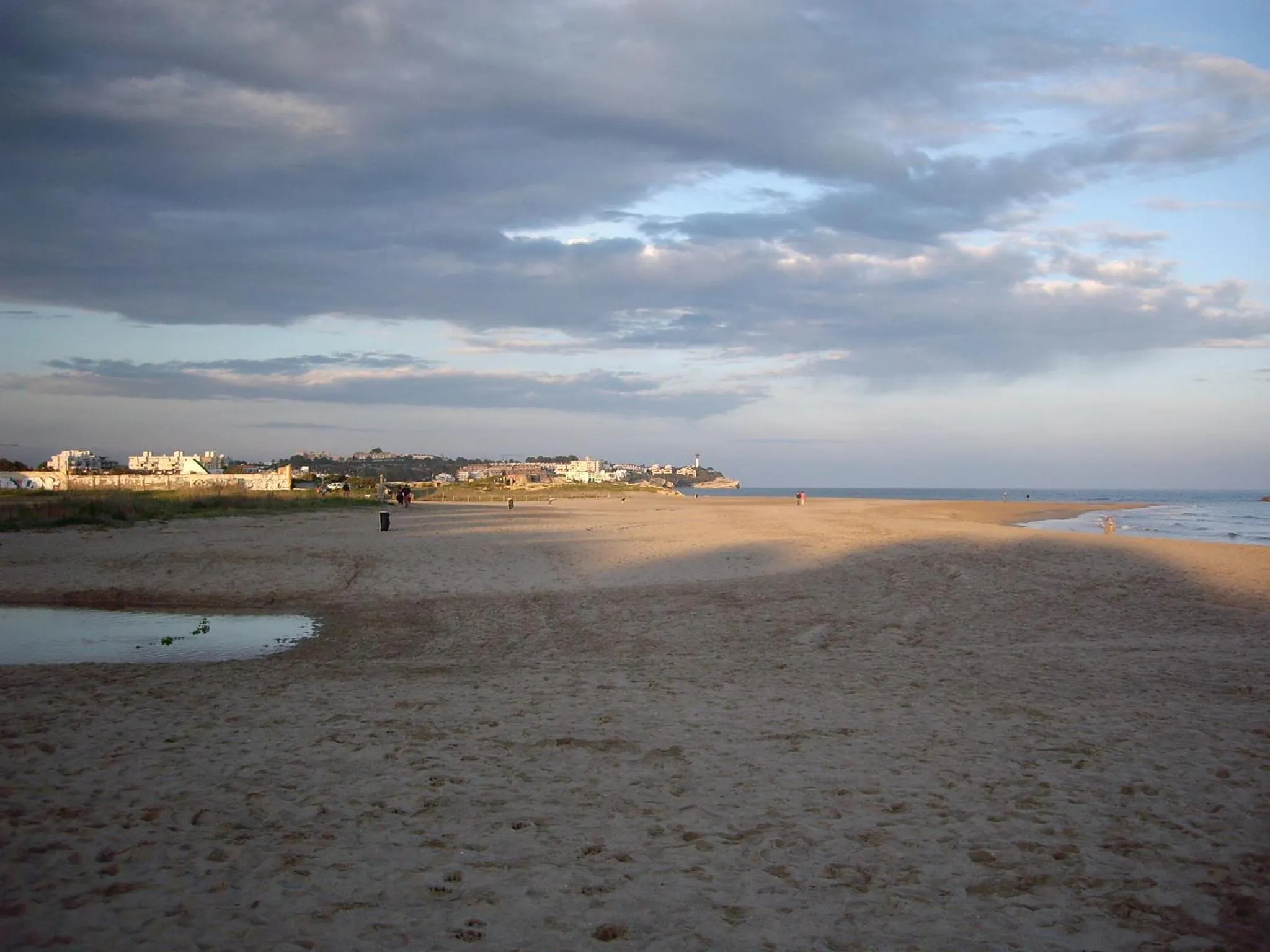 Vaste plage de sable fin baignée par une lumière dorée au coucher du soleil.