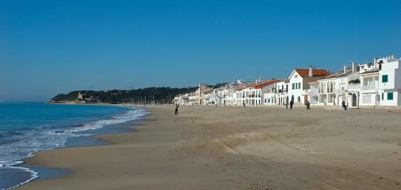 Vue d'une plage de sable fin bordée de bâtiments blancs et de végétation.