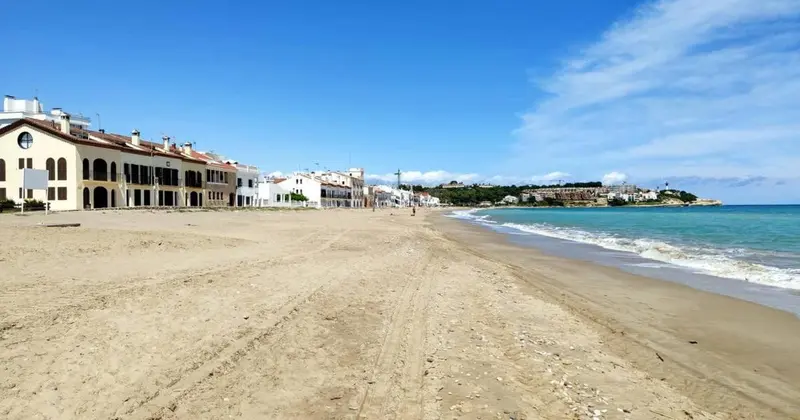 Plage de sable fin bordée d'une eau turquoise sous un ciel bleu dégagé.