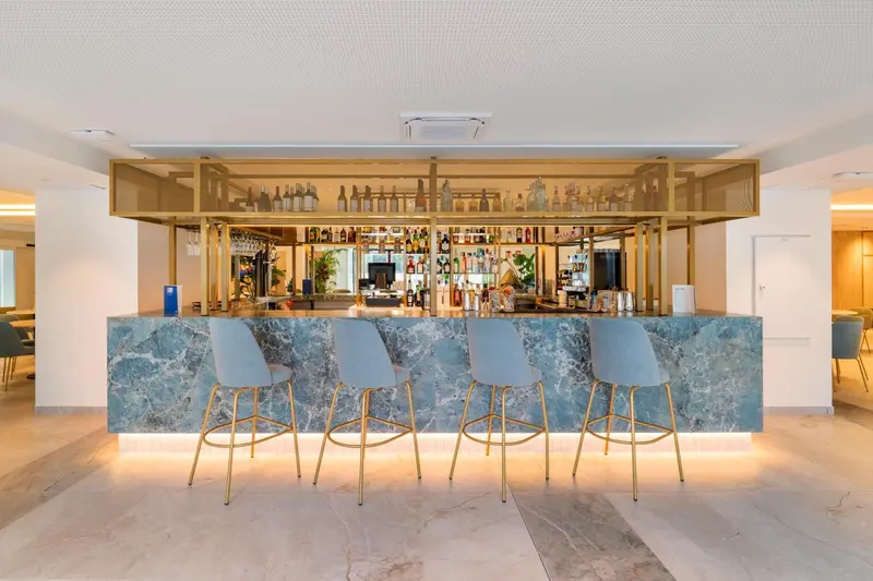 Un bar moderne avec un comptoir en marbre et des tabourets dorés.