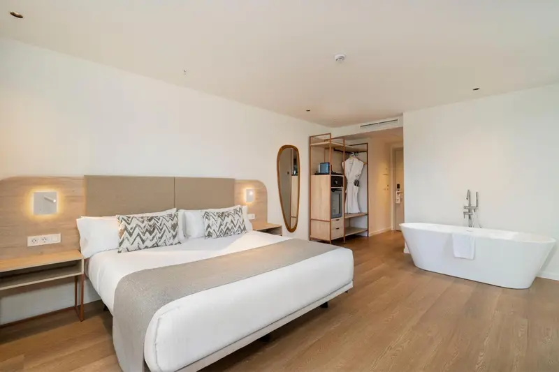 Une chambre lumineuse avec un grand lit et une baignoire îlot.