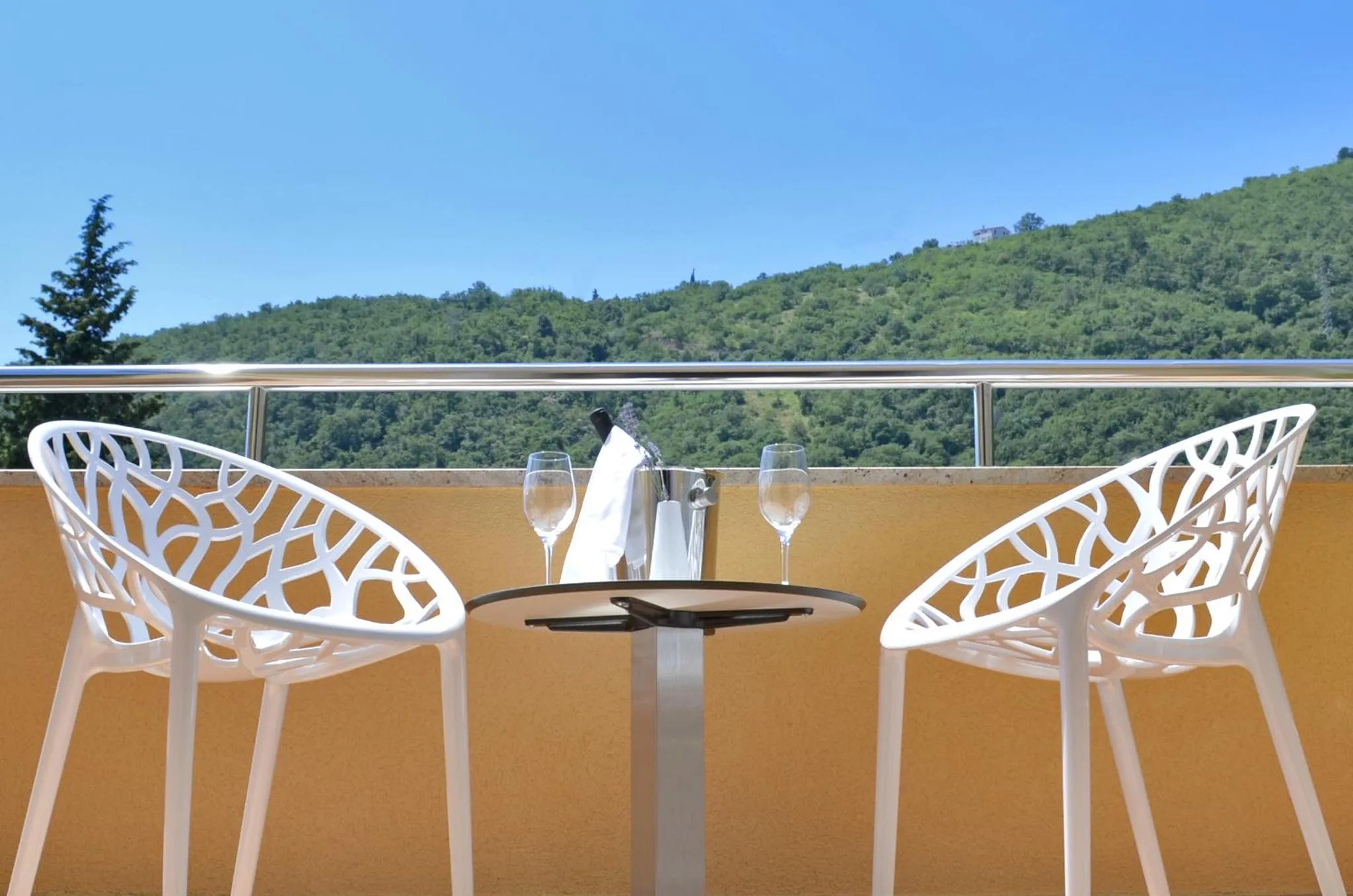 Une table est dressée avec des couverts et des verres sur une terrasse ensoleillée.
