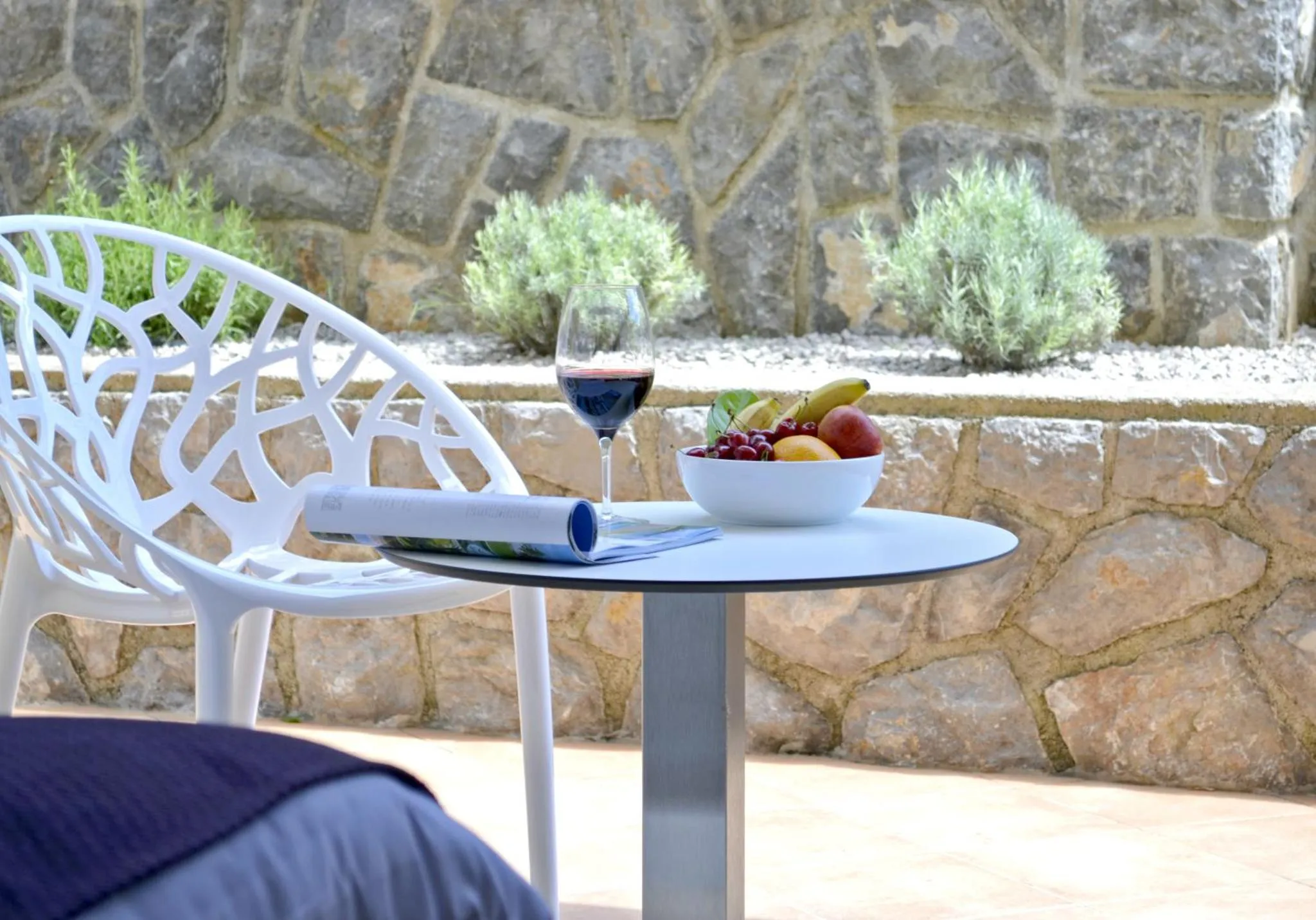 Une table basse avec un verre de vin, des fruits et un magazine sur une terrasse.