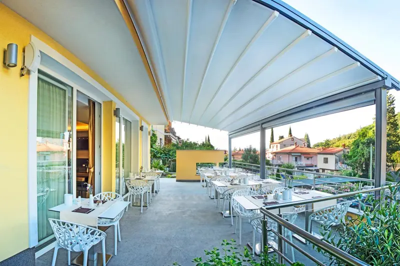 Terrasse ombragée avec tables et chaises donnant sur un paysage verdoyant.