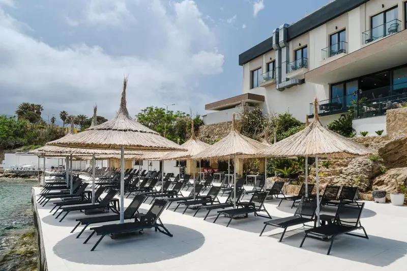 Transats et parasols de paille sur une terrasse ensoleillée avec vue sur la mer.