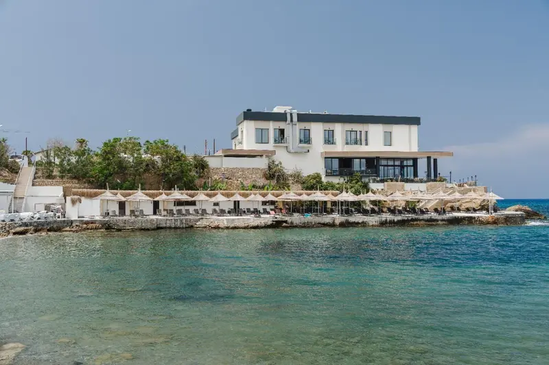 Bâtiment blanc moderne surplombant une terrasse avec transats au bord de la mer.