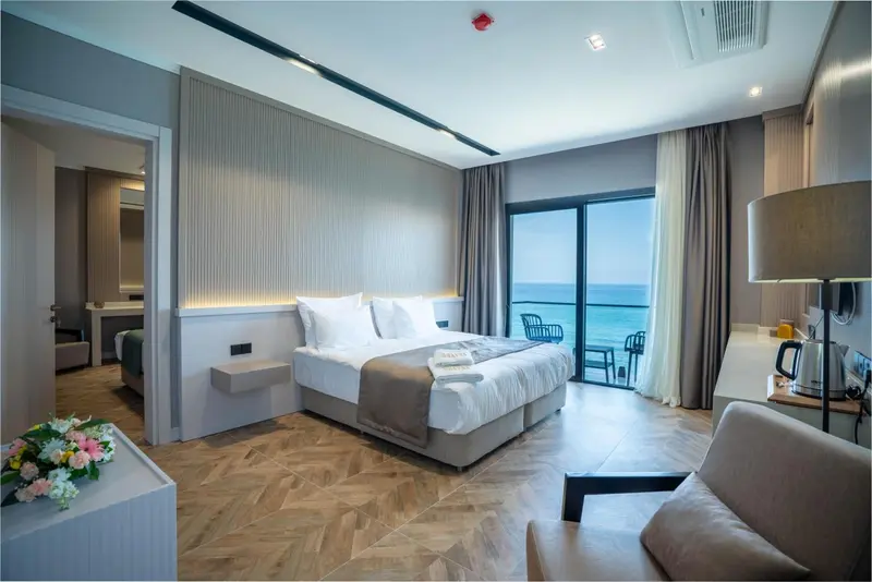 Une chambre lumineuse avec un grand lit et un accès à un balcon avec vue sur la mer.