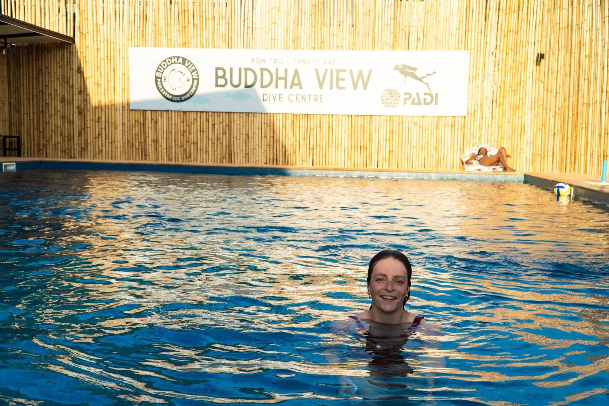 Une personne souriante émerge d'une piscine turquoise ensoleillée.