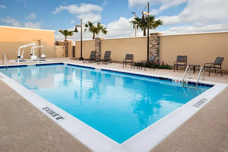 Une piscine rectangulaire entourée de chaises longues et de palmiers.