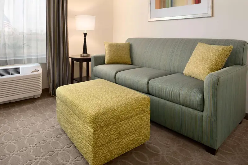 Un canapé vert avec des coussins jaunes se trouve devant un pouf assorti dans une pièce lumineuse.