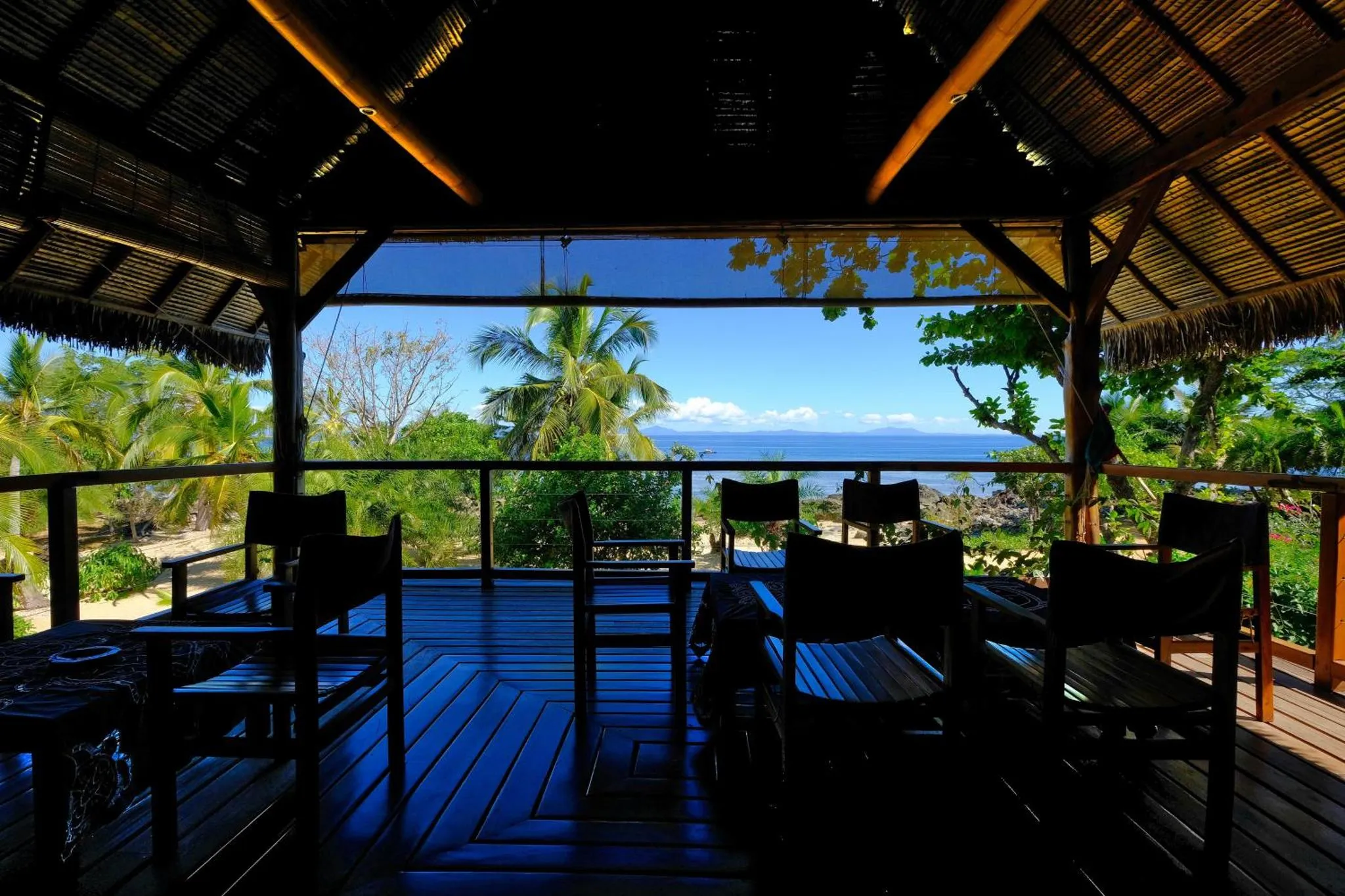Terrasse en bois sombre avec mobilier donnant sur une vue mer et végétation tropicale.