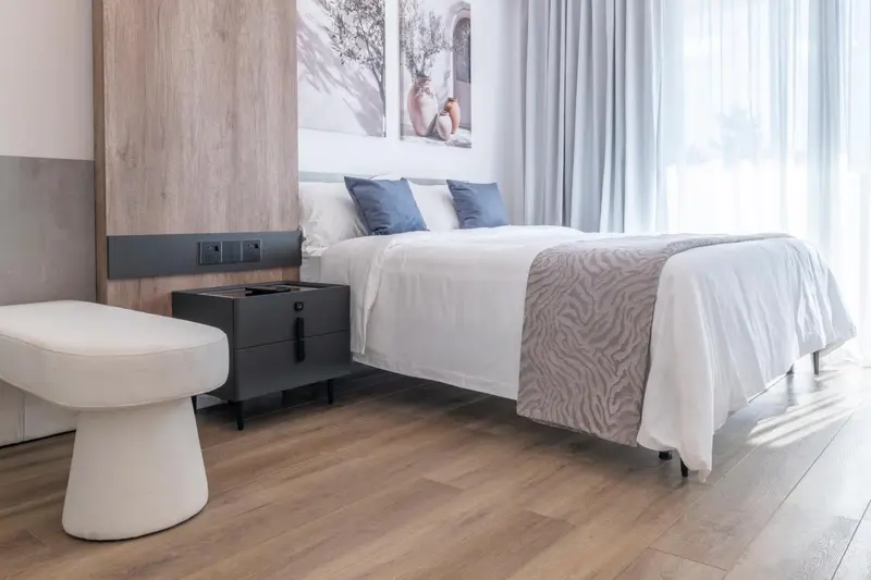 Une chambre lumineuse avec un grand lit recouvert de linge blanc et de coussins bleus.