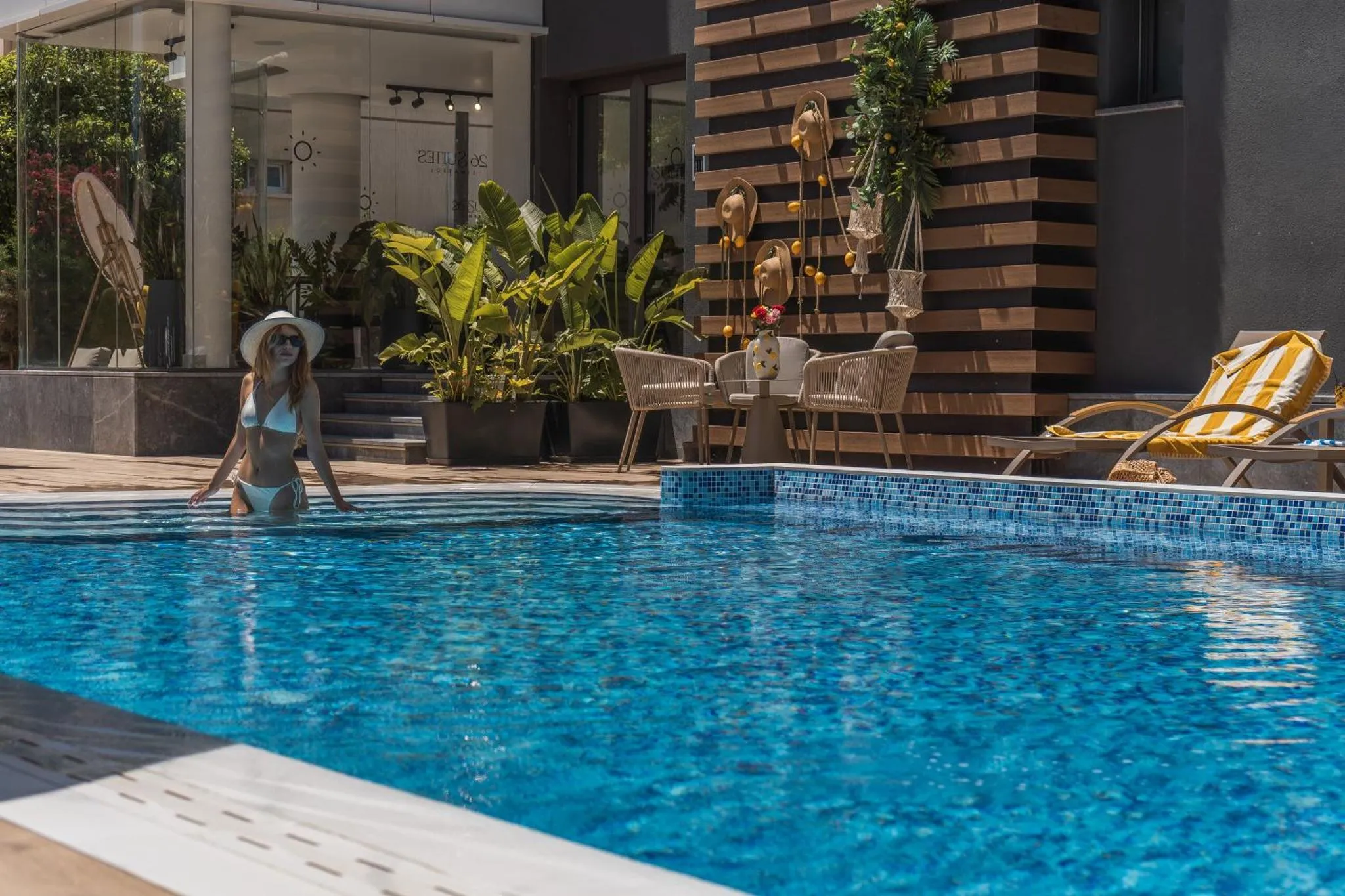 Une femme sort d'une piscine bordée de chaises longues et de plantes.