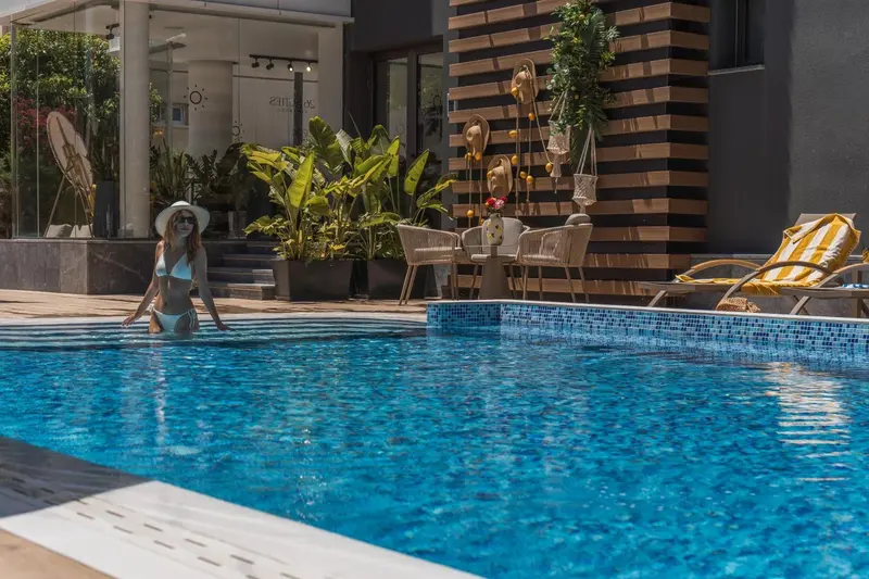 Une femme sort d'une piscine bordée de chaises longues et de plantes.