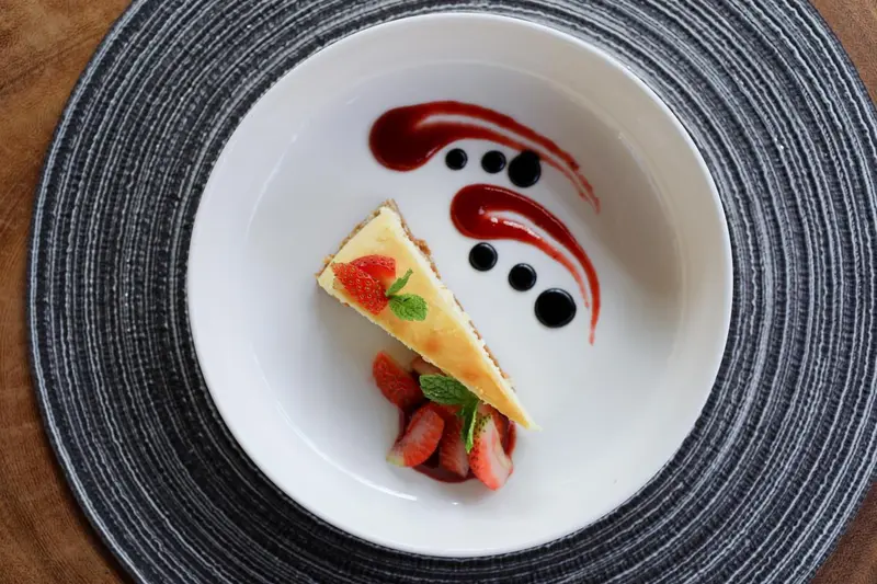 Une part de cheesecake décorée de fruits rouges est présentée sur une assiette blanche.