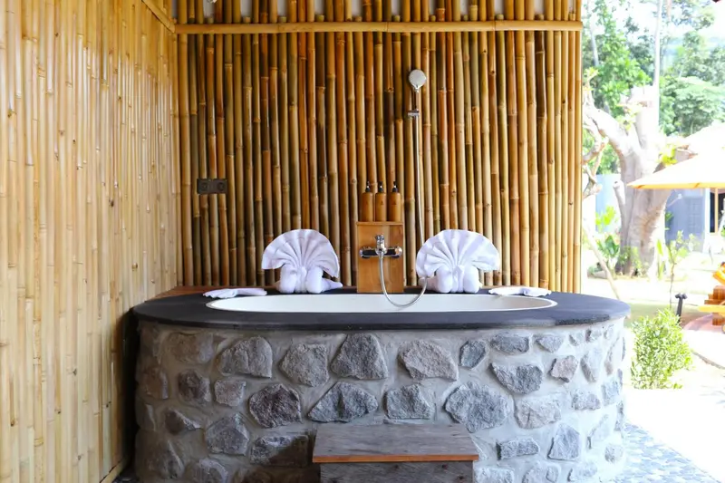 Une baignoire ronde en pierre est intégrée dans une douche extérieure en bambou.