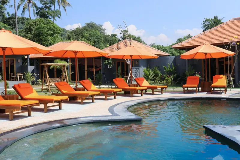 Transats orange disposés autour d'une piscine turquoise sous des parasols.