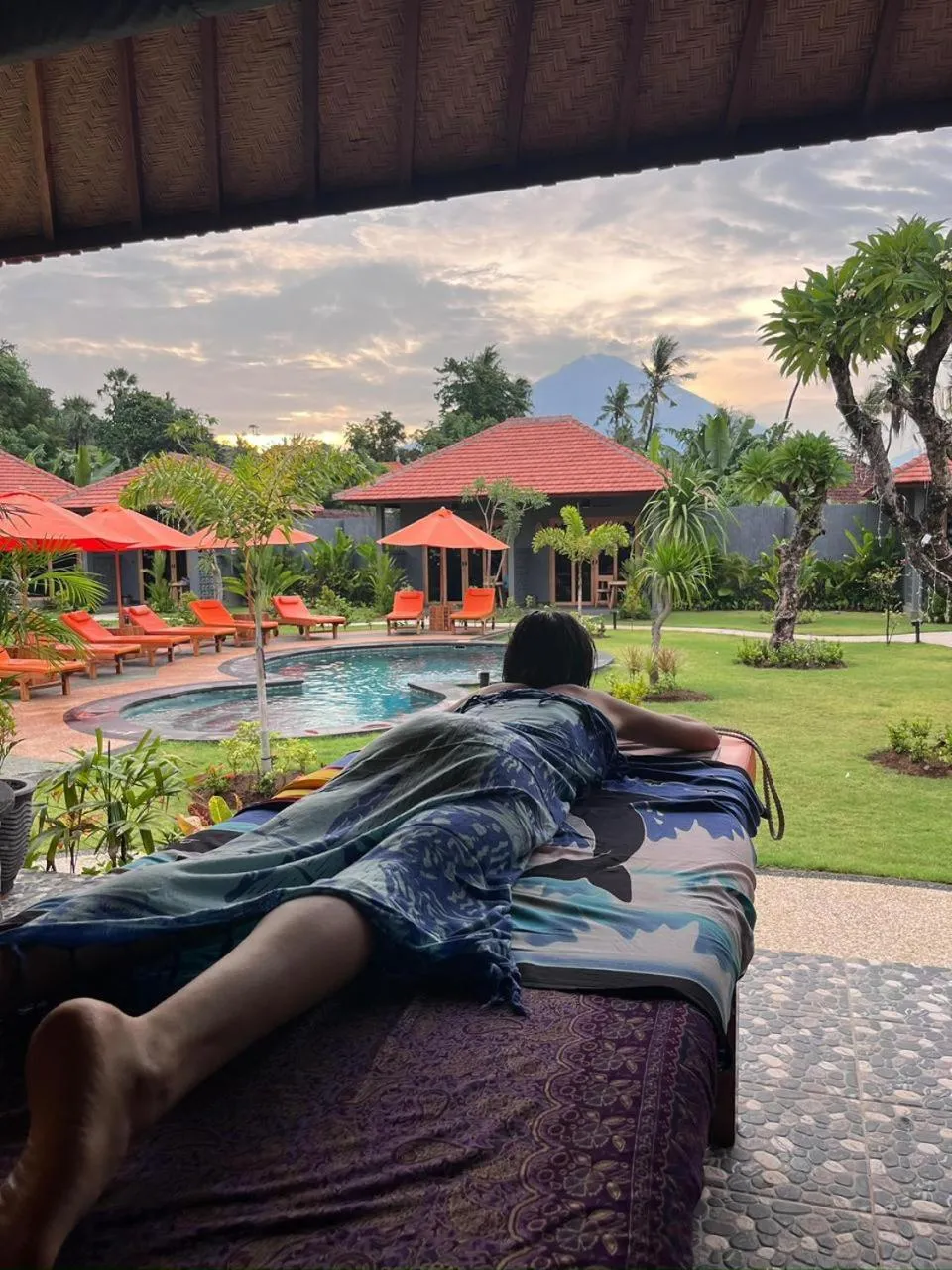 Une personne se relaxe sur un transat au bord d'une piscine dans un jardin tropical.