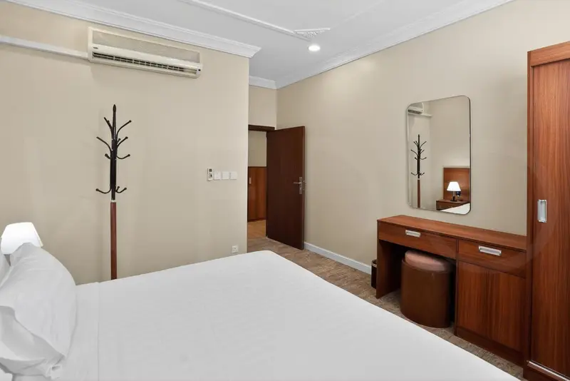 Une chambre lumineuse avec un lit blanc et un meuble en bois.