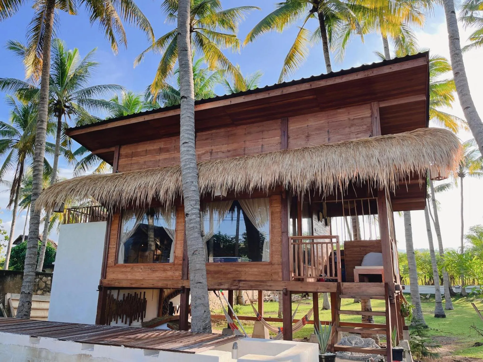 Cabane en bois sur pilotis avec terrasse et végétation tropicale.