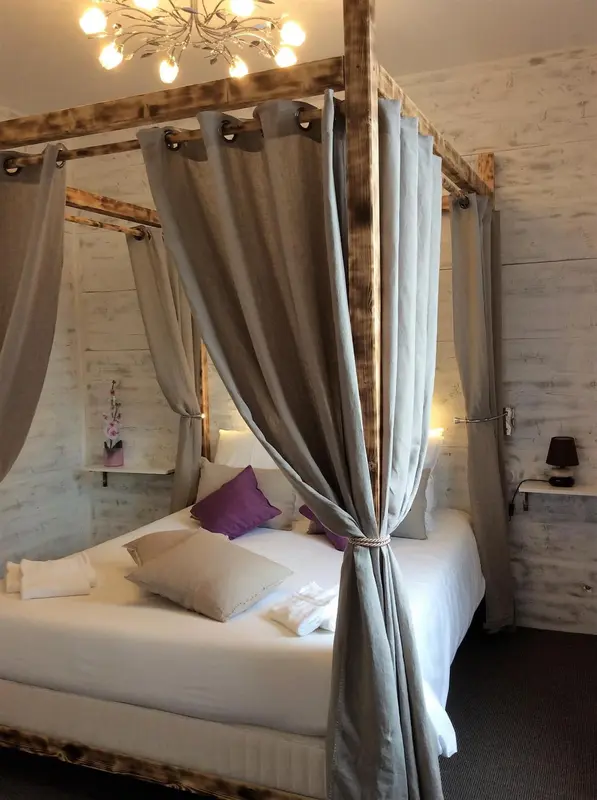 Un lit à baldaquin avec des rideaux gris et des oreillers violets dans une chambre.