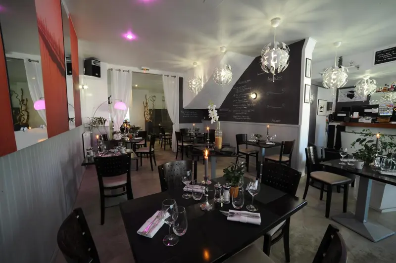 Une salle de restaurant lumineuse avec des tables dressées et des suspensions décoratives.