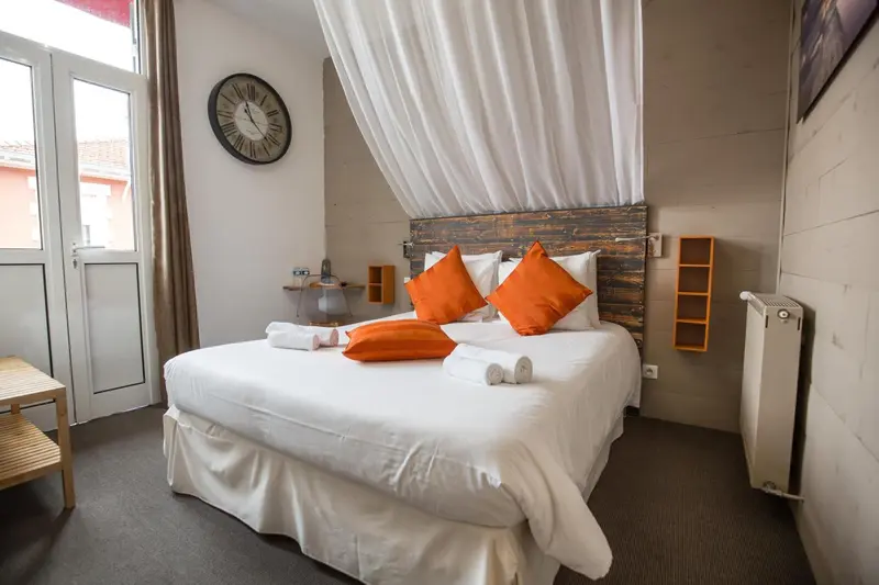 Une chambre lumineuse avec un grand lit recouvert d'une moustiquaire et des oreillers orange.
